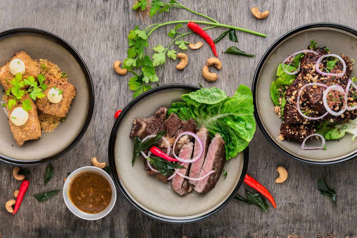Three plated beef dishes, overhead on a wooden table